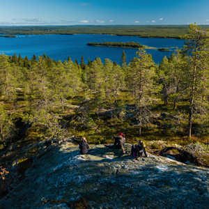 Kolme naista istuu kallioilla, joista avautuu näkymä metsään ja järvelle.