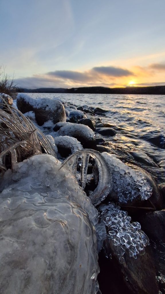 Kuvassa näkyy läheltä rantaan muodostuneita jääkiteitä. Taustalla näkyy Kipari ja Keyritty-järvi. Aurinko laskeutuu.