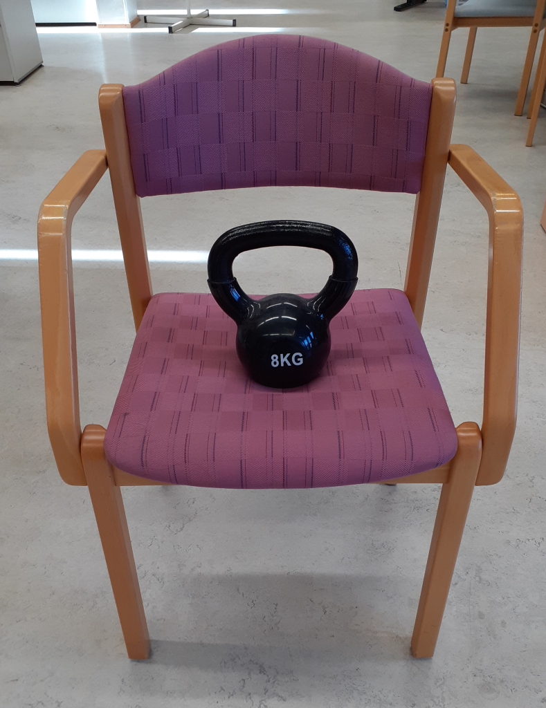 Kuvassa näkyy tuoli, jonka päällä on kahvakuula.